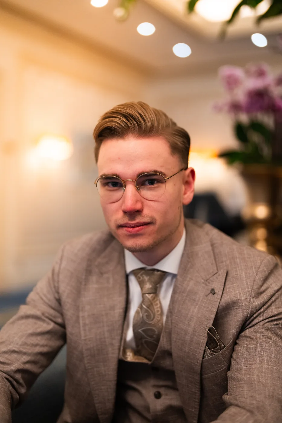 Nicholas Bode, Blick in die Kamera, beiger Anzug mit Krawatte, warmes Licht im Hintergrund