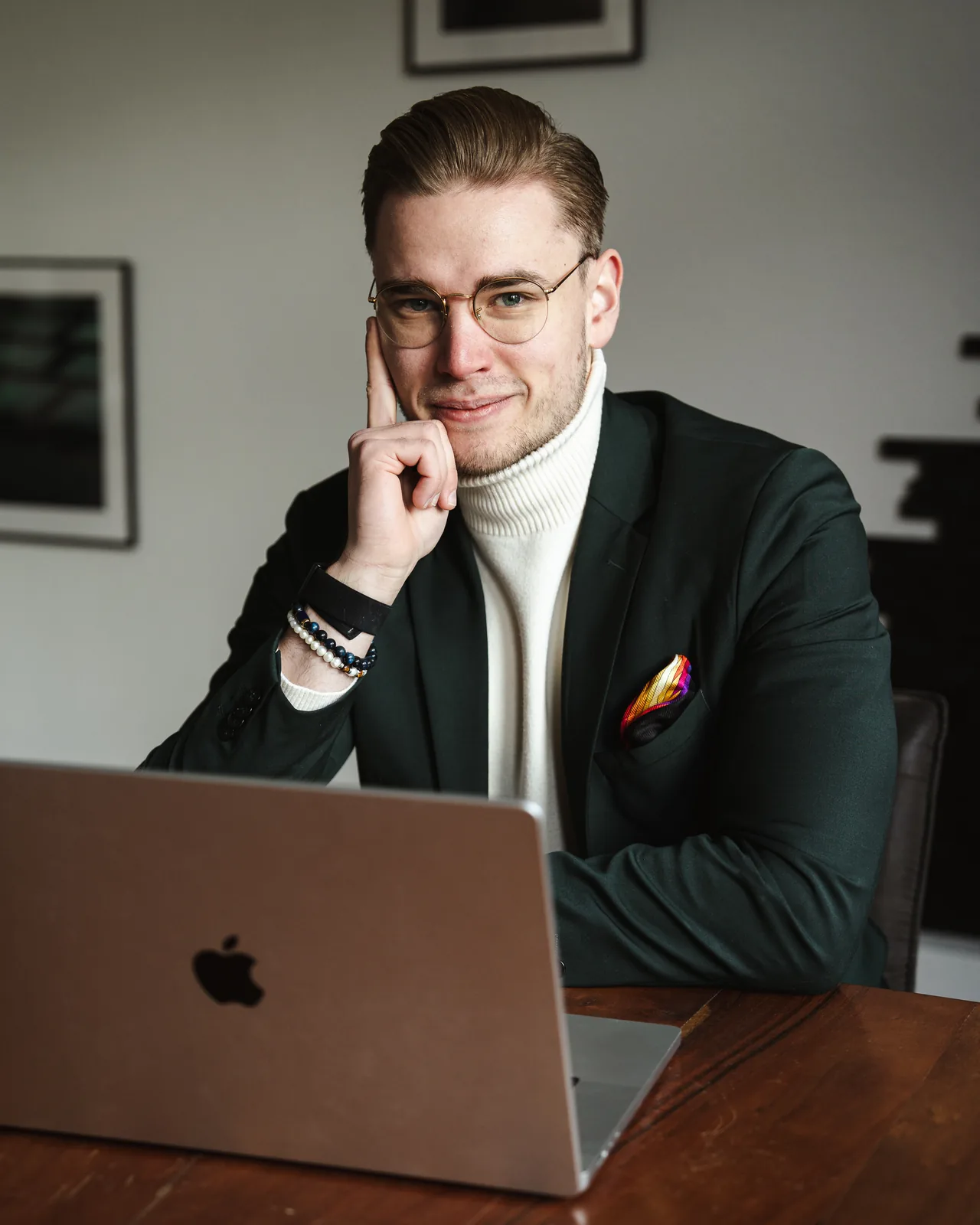 Nicholas Bode am Laptop, Hand am Kinn, Blick in die Kamera, dunkelgrünes Sakko